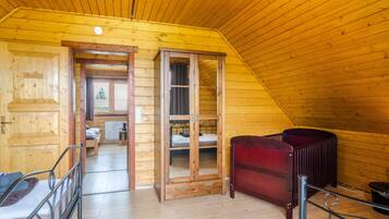 A wooden interior with a bed, a red cabinet, and a view through a door to another room.