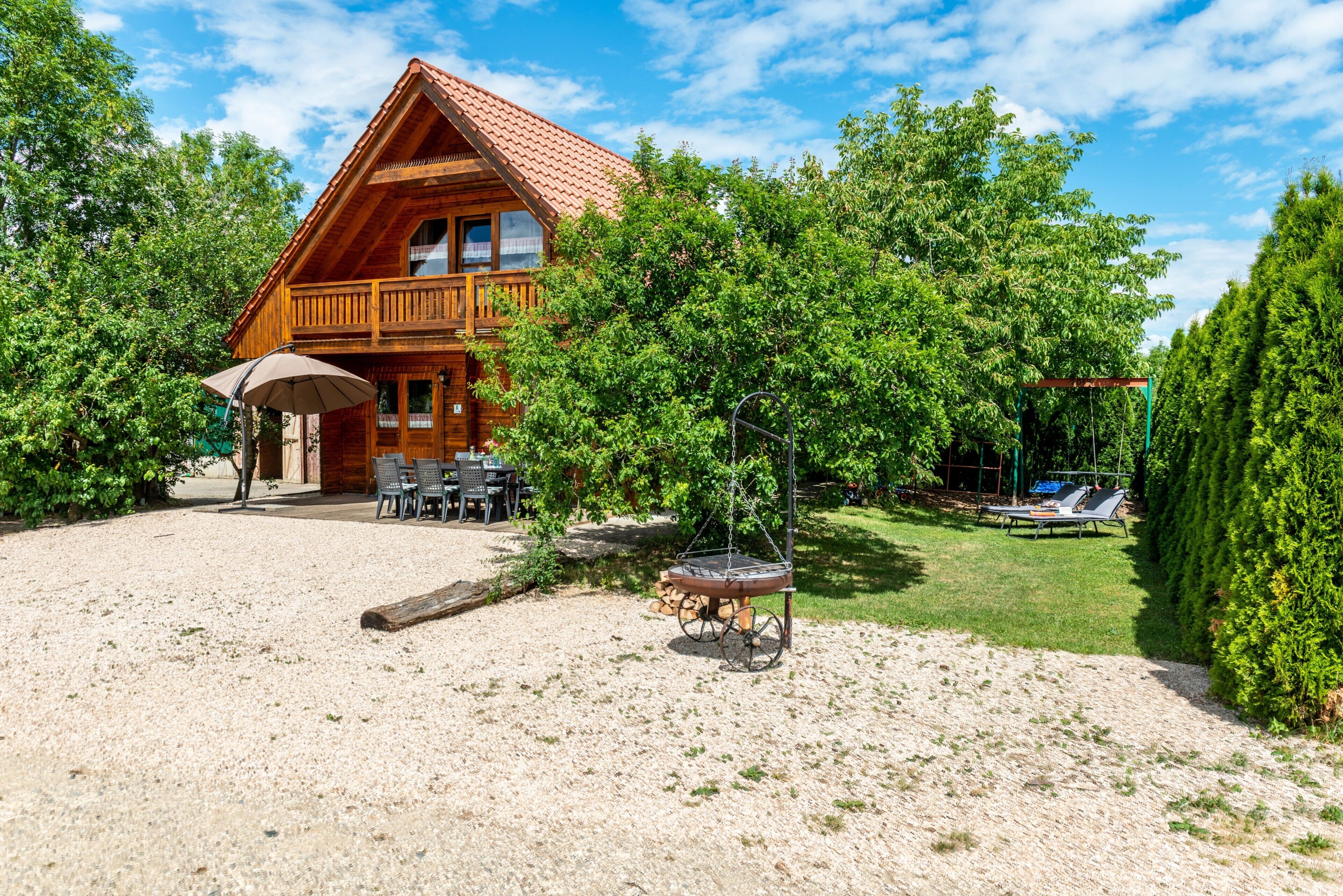 A wooden cabin with a balcony, a patio with outdoor furniture, and a swing set.