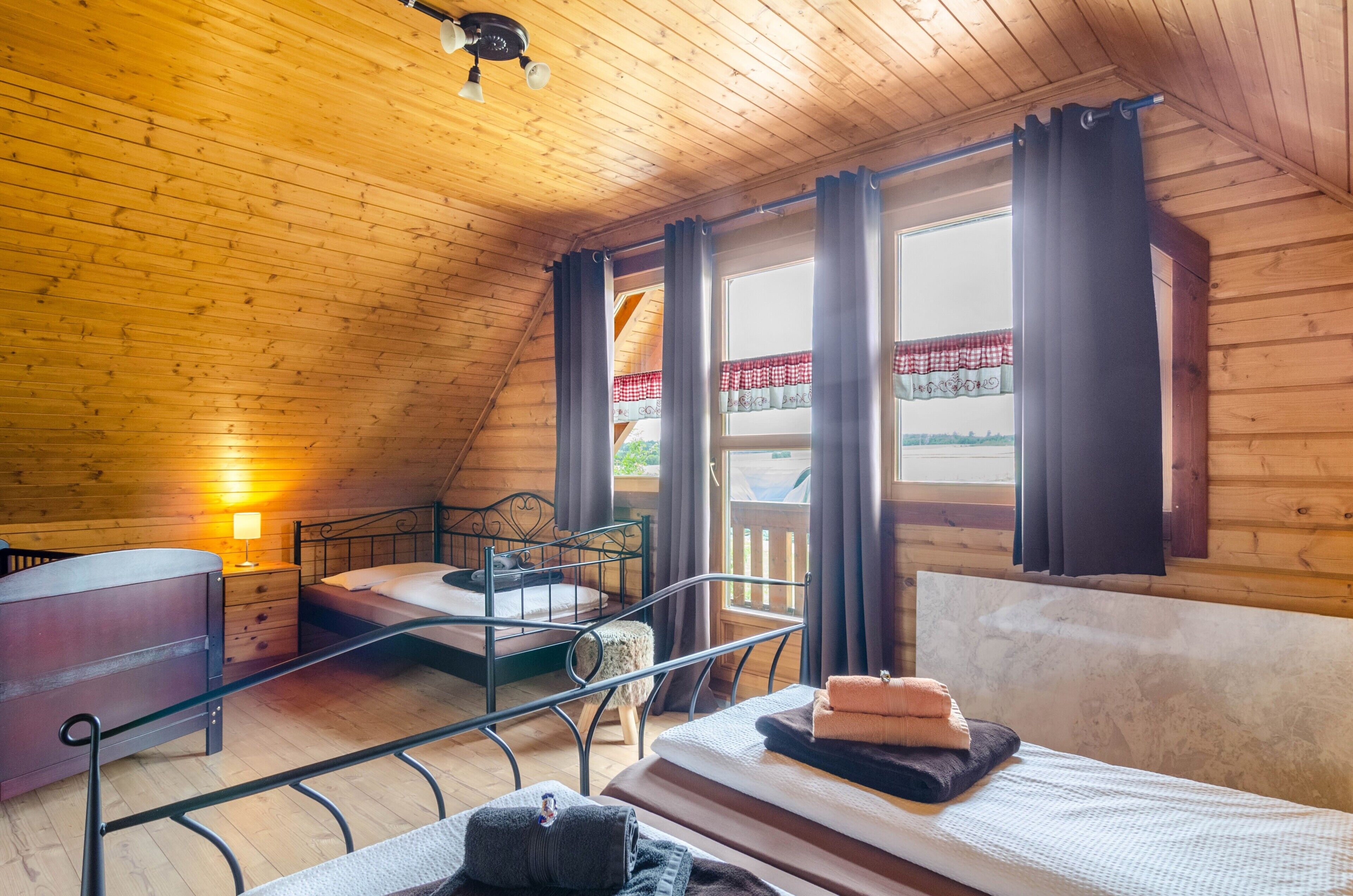 A wooden cabin room with a bunk bed, a nightstand, a lamp, and a window with curtains.