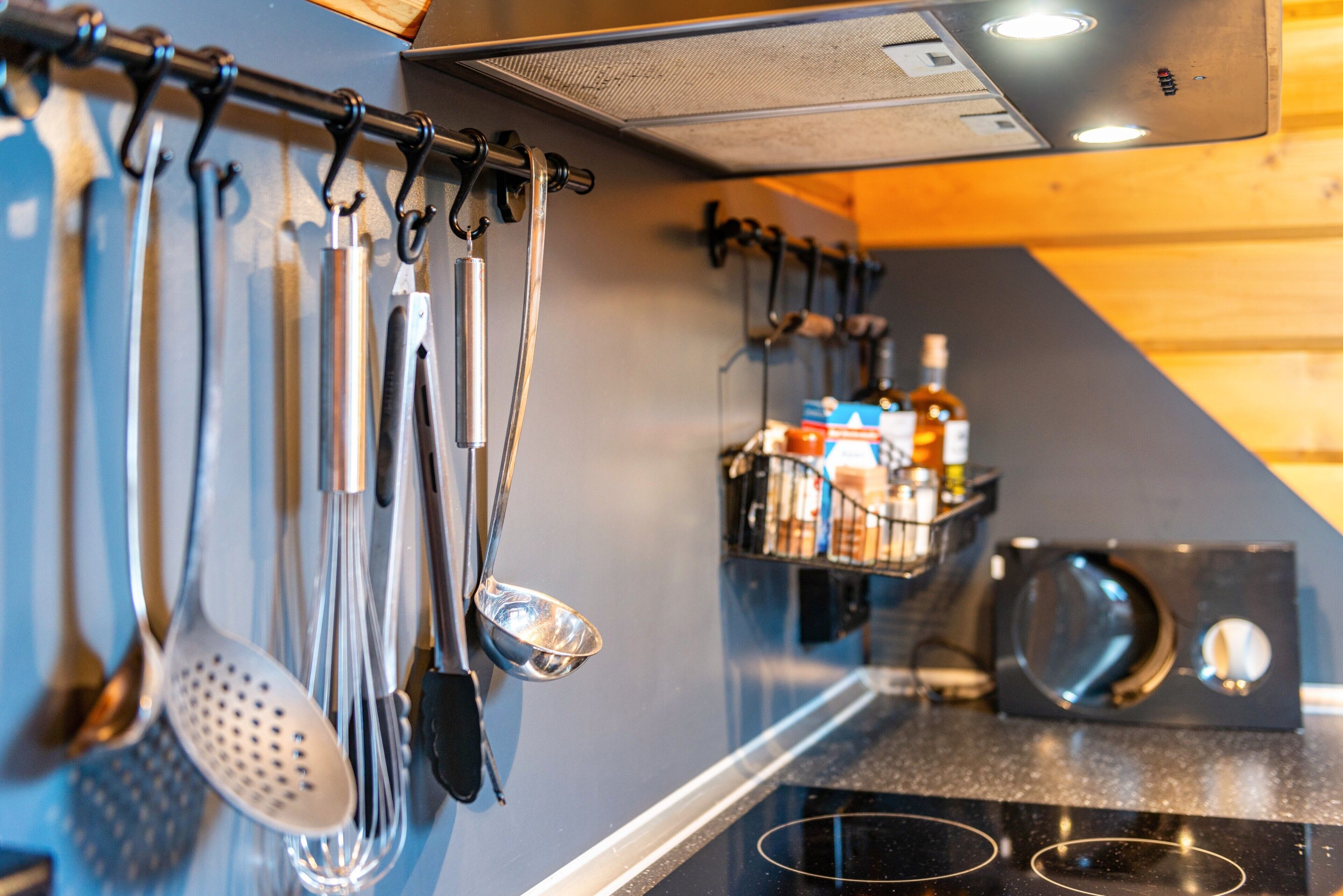 A kitchen with utensils hanging on a rack, a microwave, and a spice rack.