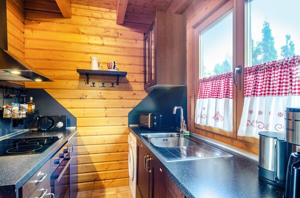 A kitchen with wooden walls, a stove, a sink, and a window with a checkered curtain.