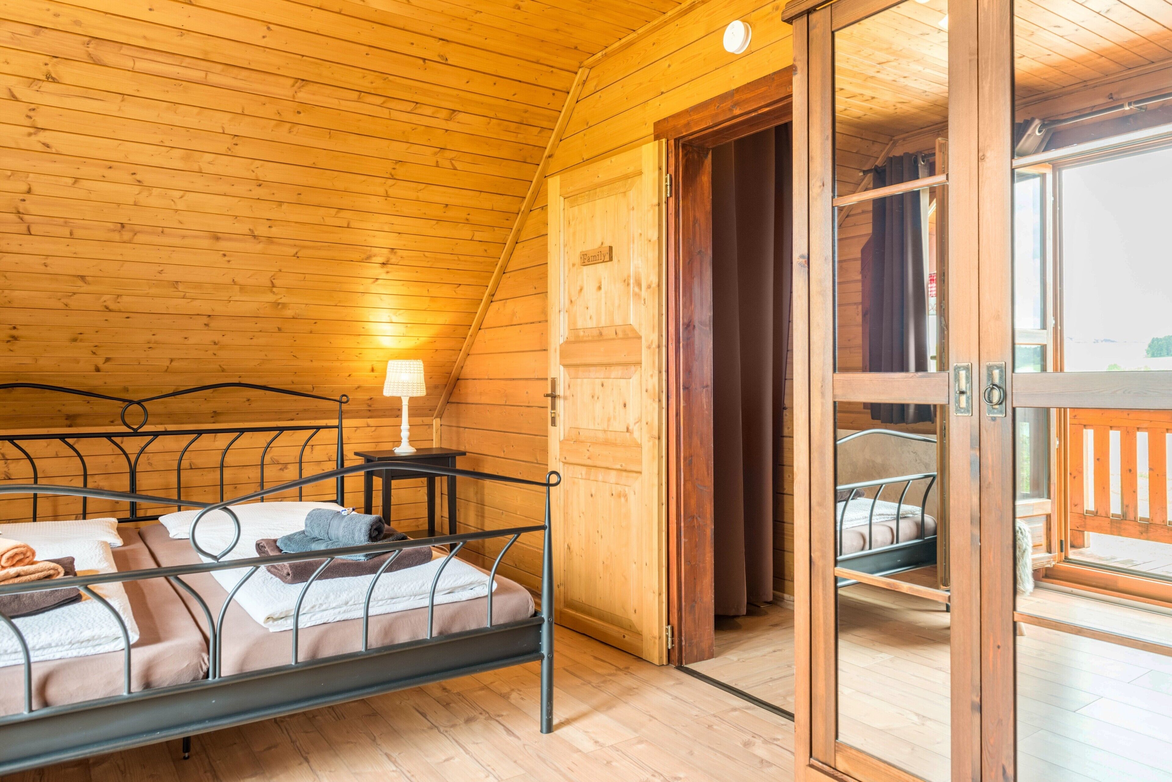 Una cabaña de madera con una cama, una mesita con una lámpara y un ventanal corredero que da a un espacio al aire libre.