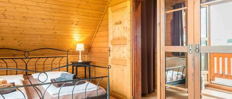 Una cabaña de madera con una cama, una mesita con una lámpara y un ventanal corredero que da a un espacio al aire libre.
