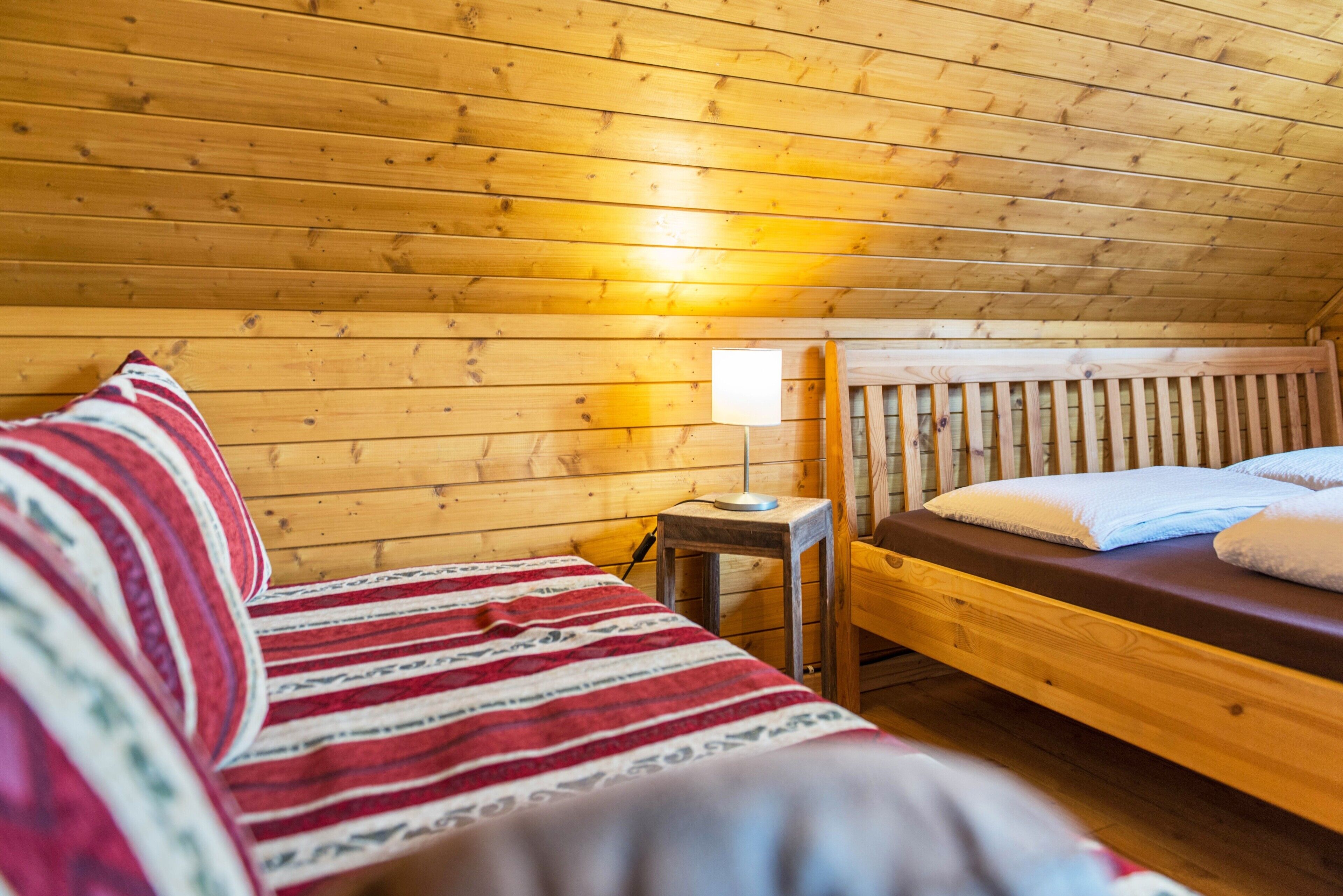 Une pièce dans une cabane en bois, comprenant un lit, une petite table et une lampe.