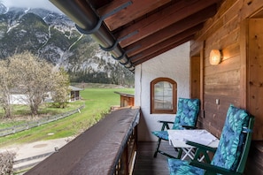 A wooden balcony with a table and chairs, a window, and a view of a mountainous landscape.