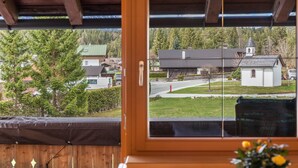A wooden-framed window with a view of a residential area, including houses and a church.