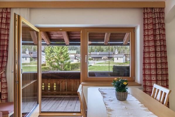 A room with a wooden ceiling, a sliding glass door, a table with a white tablecloth, and a potted plant.