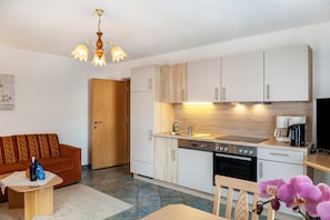 Cocina compacta con lavavajillas, horno y cafetera, junto a un sofá y una mesa de comedor.