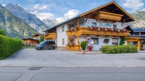 Ein Berggasthof mit Balkon, der mit Blumen geschmückt ist, ein Auto vor der Tür und ein Berg im Hintergrund.
