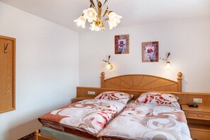 A bedroom with a wooden headboard, two bedside tables, a bed with floral bedding, a chandelier, and two wall-mounted light fixtures. - Apartment "Sterngucker Suite" with Mountain View, Shared Garden and Wi-Fi (Leutasch)