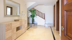 A hallway with a wooden staircase, a large mirror, a decorative console table, and a potted plant.