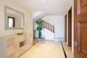 A hallway with a wooden staircase, a large mirror, a decorative console table, and a potted plant.
