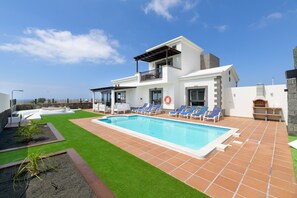 A modern two-story house with a swimming pool, outdoor seating, and a clear view of the sea.