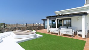 A modern outdoor patio with a stone wall, white furniture, and a view of the ocean.