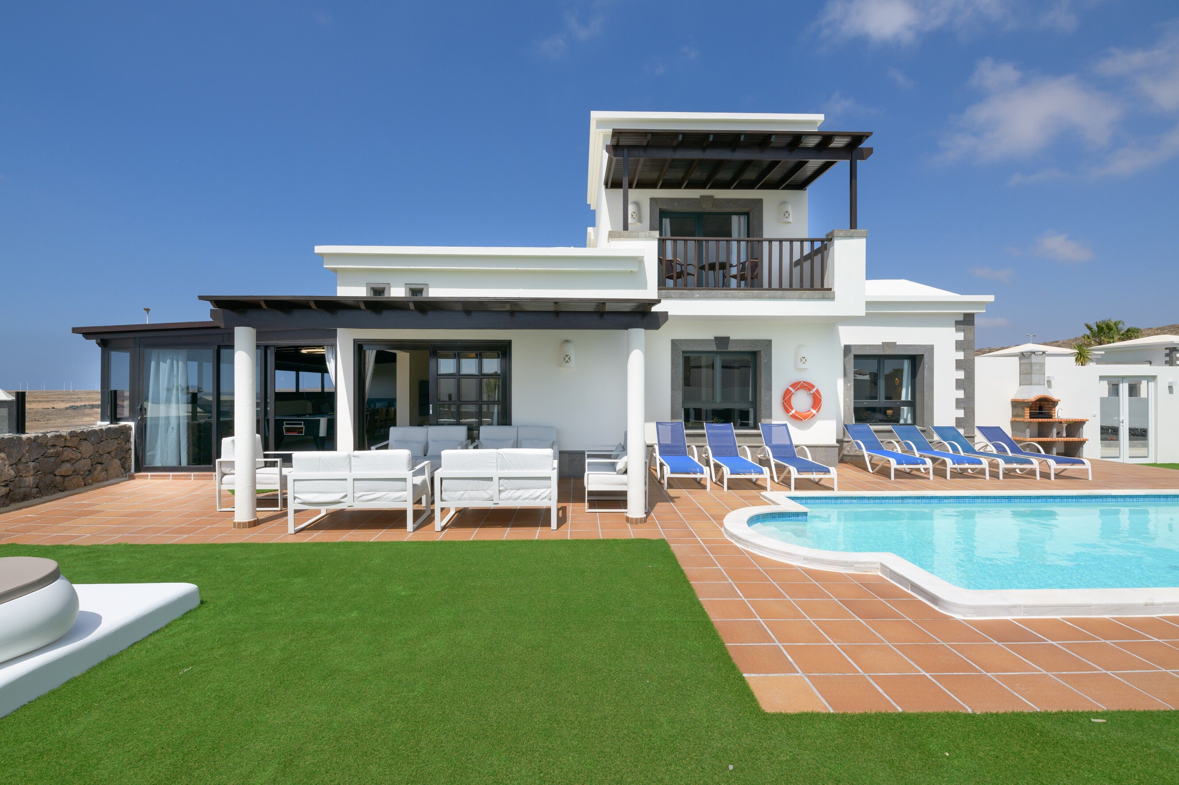 A modern two-story house with a swimming pool, outdoor seating, and a clear view of the ocean.
