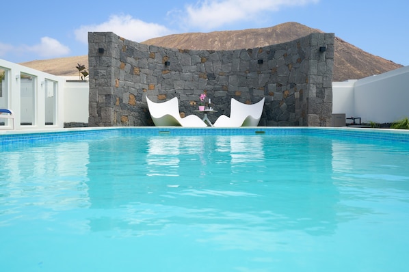 A swimming pool with a stone wall and a mountain in the background.