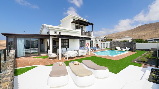 A modern house with a swimming pool, outdoor seating, and a view of the hills.
