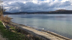 Blick auf einen See mit einer Bank, ruhigem Wasser und entfernten Hügeln.