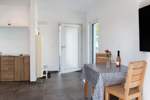 Un coin repas comprenant une table, des chaises, une bouteille de vin et un vase avec des fleurs.