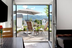 Puerta corrediza de vidrio abierta que da a un patio al aire libre con una mesa, sillas y una sombrilla.