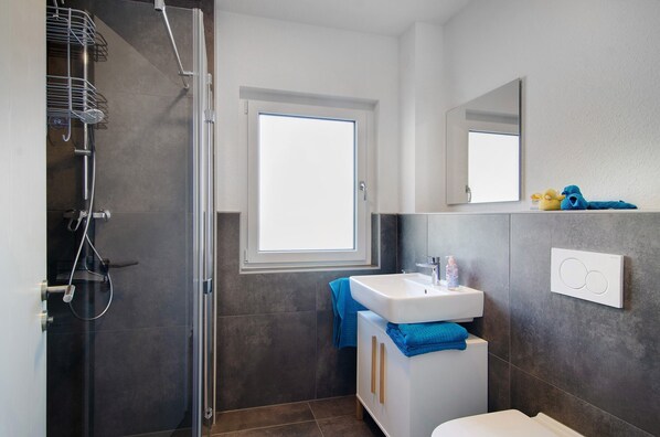 Un baño moderno con ducha, lavabo, espejo y ventana.