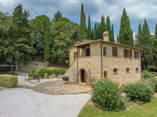 A stone building with a stone staircase, a covered patio, and a view of tall trees.