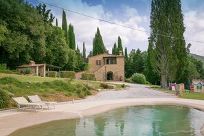 Una casa de piedra con piscina, rodeada de exuberante vegetación y árboles altos.