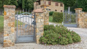 A stone house with a metal gate, surrounded by greenery and a gravel driveway. - Villa Podere Cafaggio with Private Pool, Terrace, and Air Conditioning (Monteverdi Marittimo)