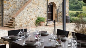 A stone building with a staircase, outdoor dining area with tables and chairs, and a view of greenery. - Villa Podere Cafaggio with Private Pool, Terrace, and Air Conditioning (Monteverdi Marittimo)