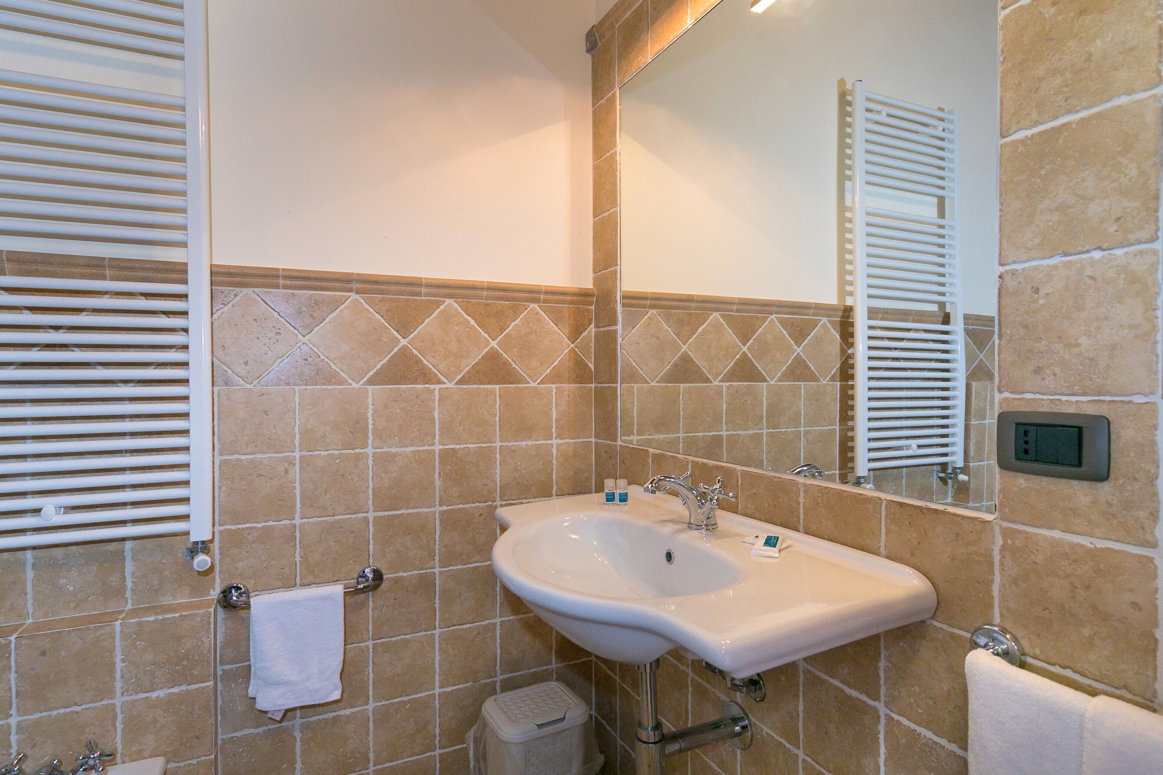 Une salle de bain équipée d’un lavabo, d’un miroir, d’un porte-serviettes et d’une petite poubelle.
