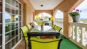 A covered patio with a glass table and chairs, a grill, and potted plants.