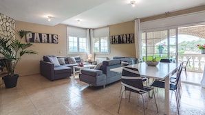 A spacious living area with a sofa, dining table, chairs, and a potted plant.