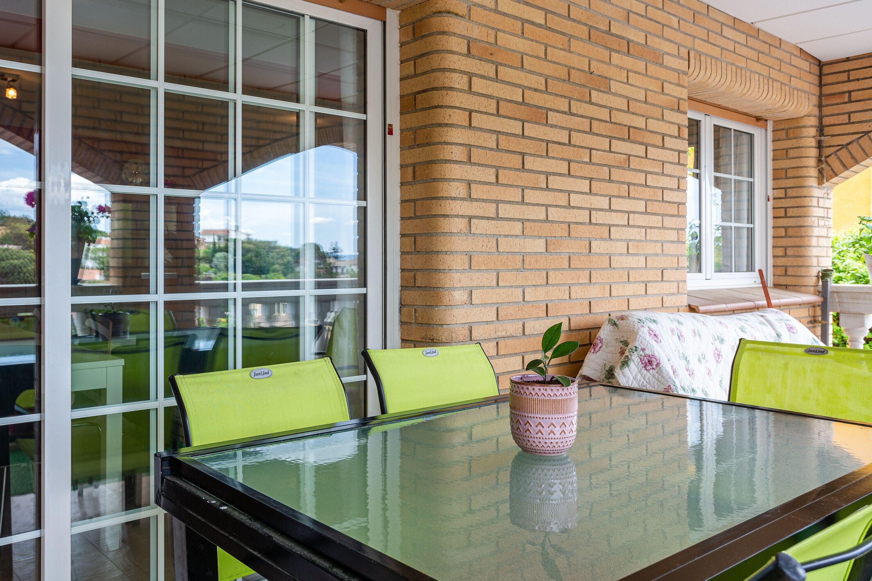A glass-top table with chairs, a potted plant, and a brick wall.