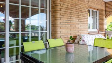 A glass-top table with chairs, a potted plant, and a brick wall.