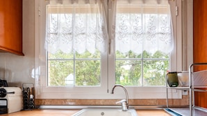 A kitchen with a sink, window with curtains, and a rack with bottles.
