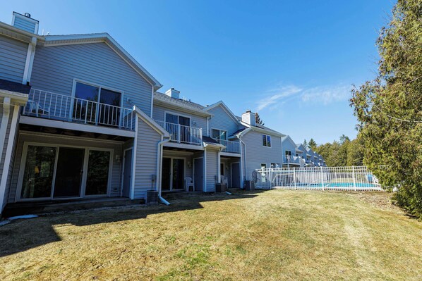 A multi-story residential building with a front porch, a covered patio, and a fenced swimming pool area.