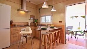 Una cocina con un refrigerador blanco, armarios de madera, un ventanal con persianas y un comedor con mesa y sillas.