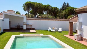Una piscina con sillas de descanso, un patio y vistas a árboles y edificios.