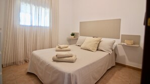 Una cama bien hecha con almohadas y toallas dobladas, una mesita de noche con una planta y un cabecero.