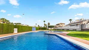 A swimming pool with a tiled edge, a grassy area, and a building with a balcony. - Holiday Home "Un Regalo de Corazón" with Shared Pool & Wi-Fi (Orihuela)