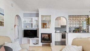 A living room with a TV, sofa, and fireplace. There is a kitchen visible in the background. - Holiday Home "Un Regalo de Corazón" with Shared Pool & Wi-Fi (Orihuela)