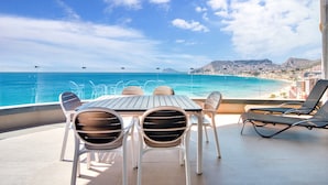 A terrace with a table and chairs, overlooking a beach and cityscape.