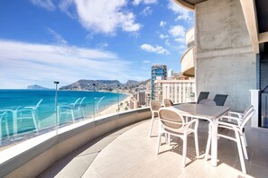 A balcony with a table and chairs, overlooking a beach and cityscape.