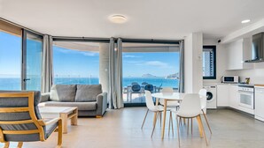 A modern living room with a sofa, chairs, a dining table, and a kitchen area with appliances.