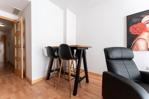 Une pièce avec un plancher en bois, un fauteuil en cuir noir, une petite table entourée de trois chaises noires, et un tableau accroché au mur.