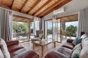 A spacious living area with a wooden ceiling, leather sofas, a glass coffee table, and large sliding glass doors leading to an outdoor patio. - Holiday Home "Casa La Plaza" with Mountain Views, Private Pool and Wi-Fi (El paso)