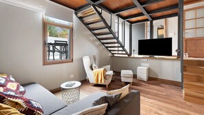 Een moderne woonkamer met een bank, fauteuil en een televisie. Een trap leidt naar een hoger niveau.