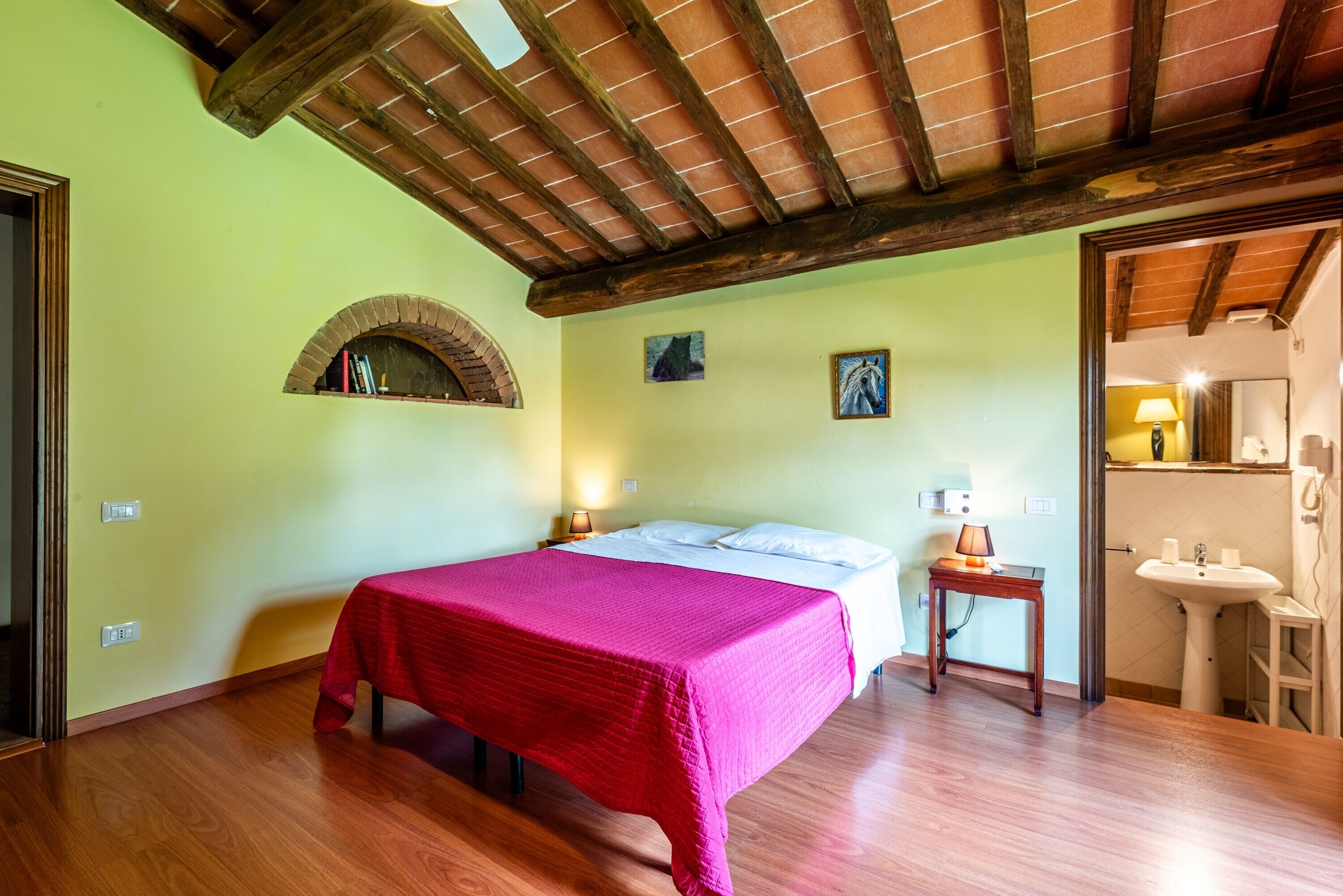 Un dormitorio con cama, mesita de noche, una pequeña mesa, un espejo y un baño con lavamanos.