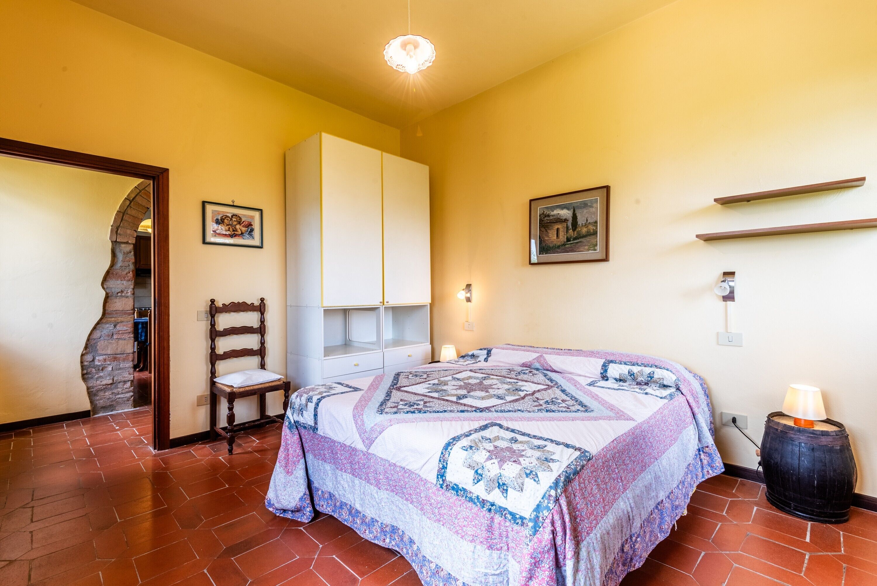 A bedroom with a bed, a chair, a wardrobe, a picture on the wall, and a lamp.