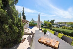 Un patio con mesa lista para cuatro, asientos al aire libre y vistas a una piscina y follaje.